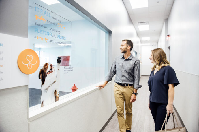Dog daycare employee giving a store tour in front of a playroom window